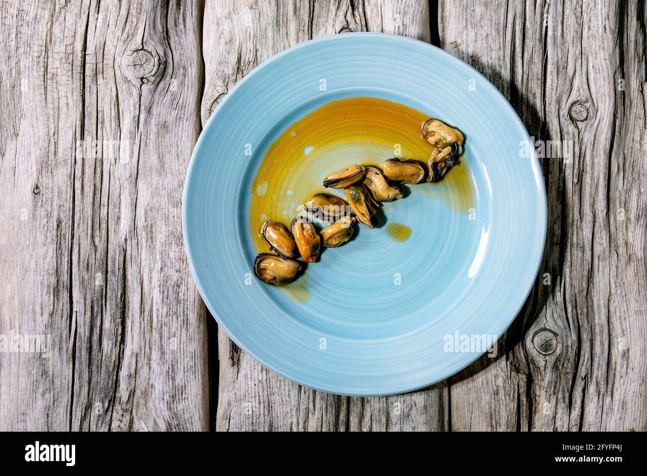 Mejillones ahumados en aceite sobre placa cerámica azul sobre fondo de madera gris antiguo. Vista superior, diseño plano. Espacio de copia Foto de stock