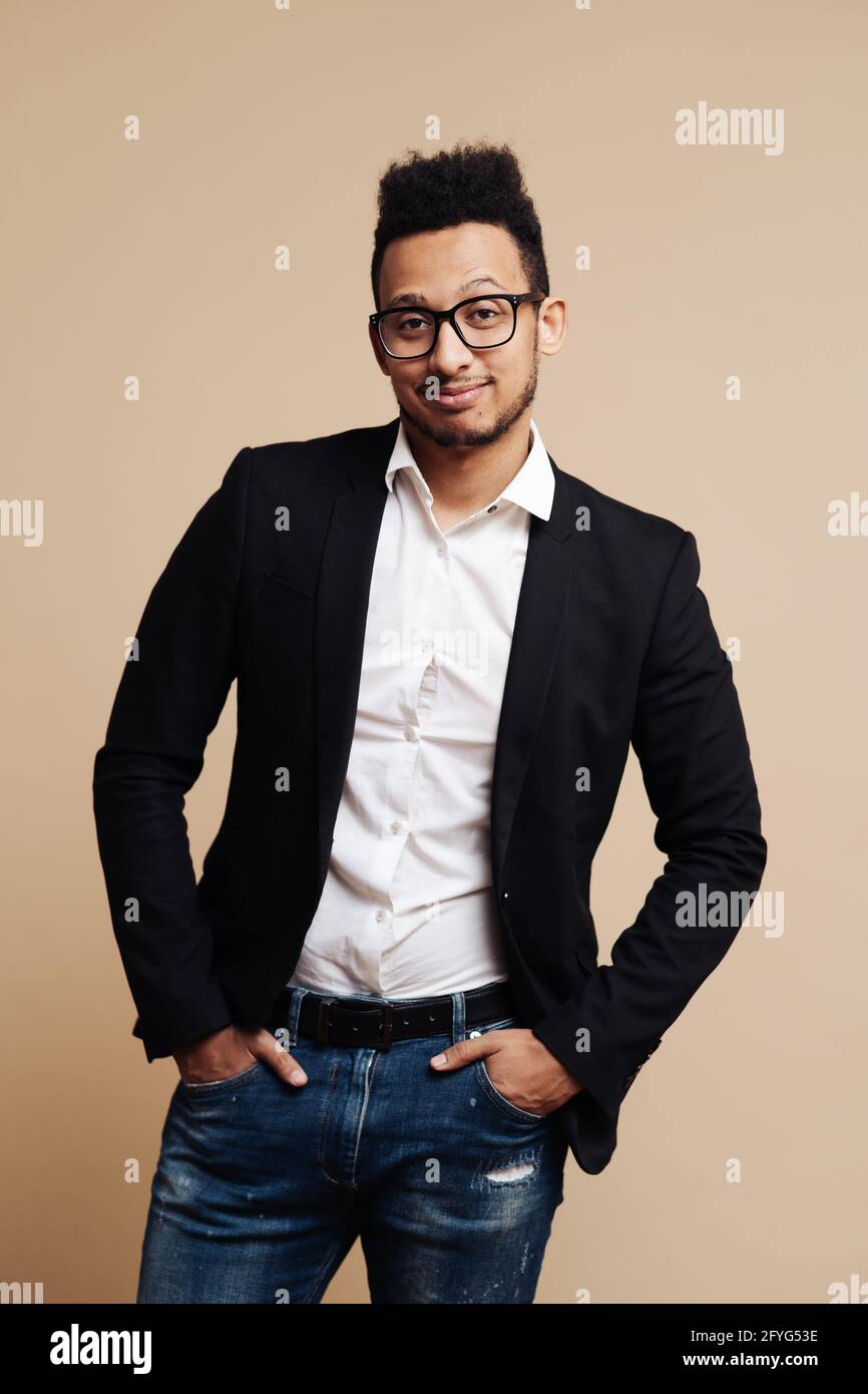 Retrato de un joven hombre de negocios afroamericano con camisa, traje negro,  gafas y mirando la cámara mientras se encuentra de pie sobre fondo beige  Fotografía de stock - Alamy