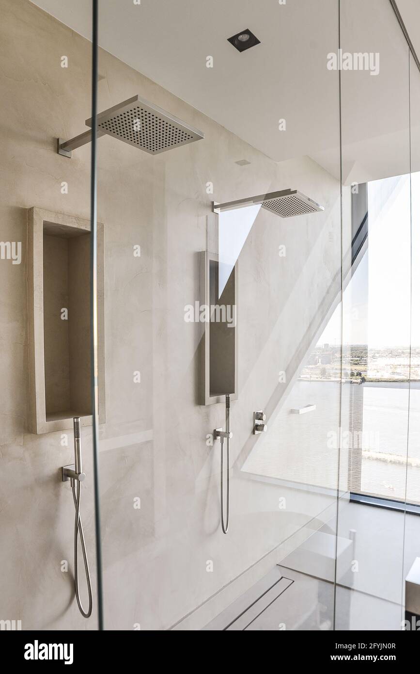 Lujosa ducha doble de lluvia en la pared de azulejos beige detrás pared de  cristal en el baño moderno Fotografía de stock - Alamy