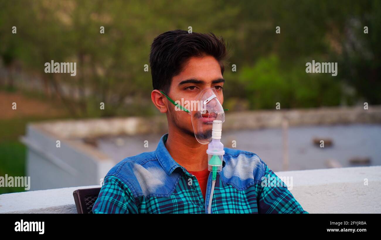 Hombre infectado con la enfermedad de Coronavirus. Paciente indio inhalando oxígeno usando máscara fuera de los hospitales. Niño adulto respirando con nebulizador sobreviviendo Foto de stock