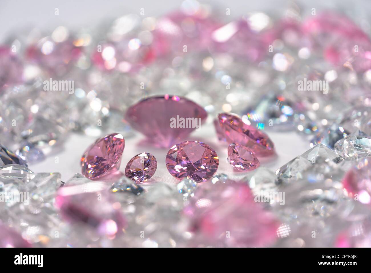 Un grupo de diamantes de color rosa dispuestos en medio de diamantes  blancos en un fondo blanco. Vista superior de diamantes de color rosa. Fondo  de diamantes blancos Fotografía de stock -