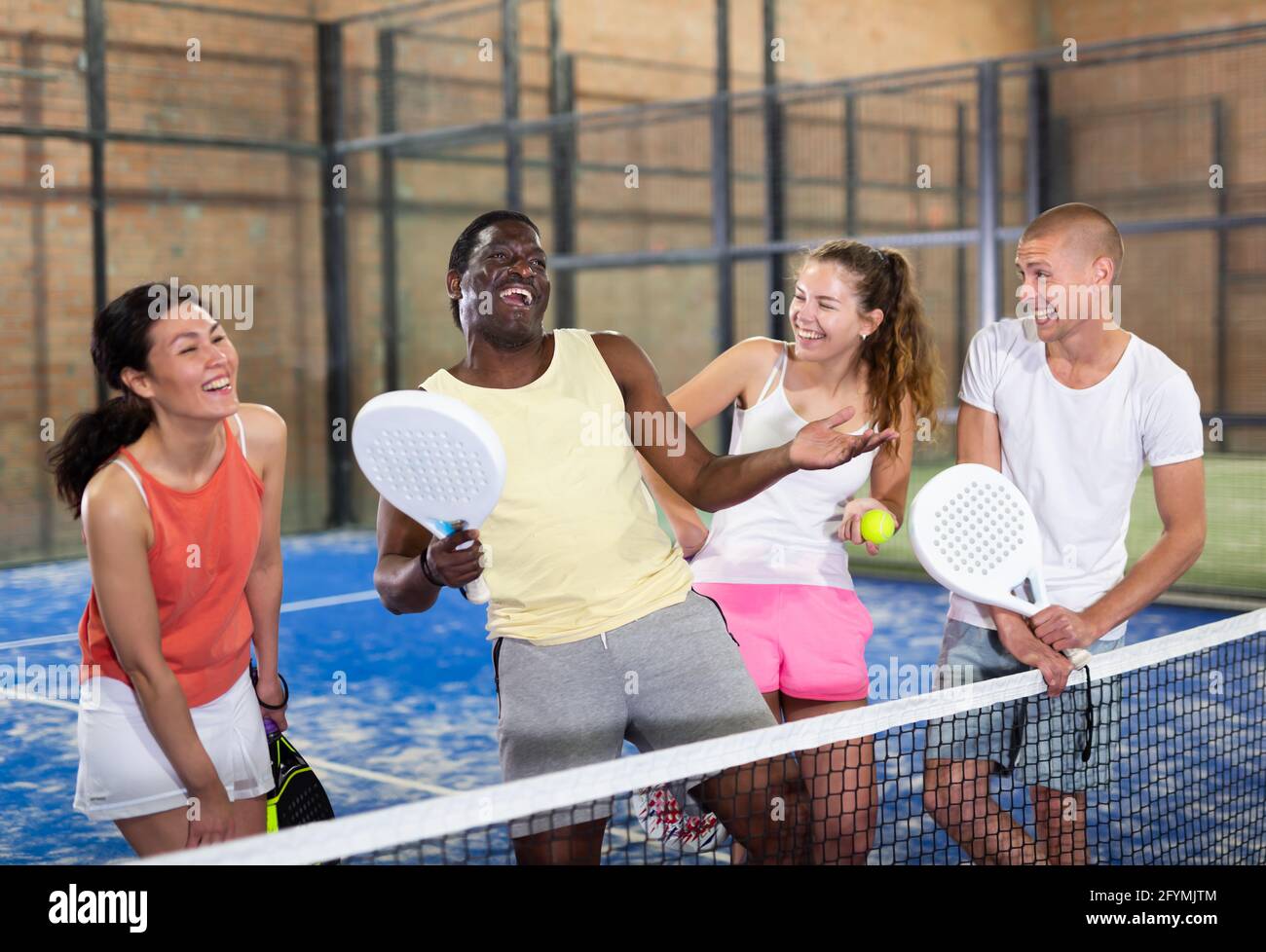 Hombres y mujeres felices de diferentes nacionalidades en ropa deportiva  con raquetas y pelotas en manos hablando amable cerca de la red en pista  interior de padel Fotografía de stock - Alamy