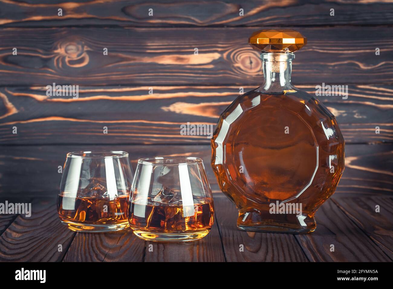 Una botella de whisky y dos vasos en una mesa de madera marrón oscuro. Bebida alcohólica amarilla transparente con hielo. Brandy, borbón. Alcohol drín fuerte Foto de stock