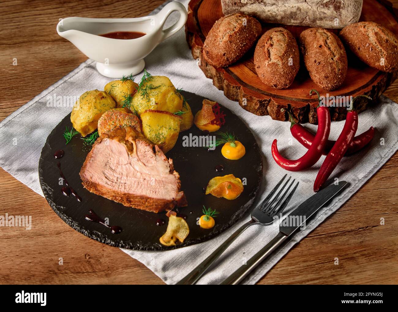 Carne con patatas al horno con eneldo, salsa y mostaza en un plato negro de  pizarra junto a chiles y bollos y pan en una tabla de madera Fotografía de  stock -