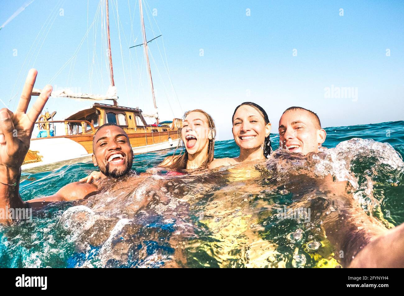 Jóvenes amigos multirraciales tomando selfie y nadando en el barco de vela viaje por el mar - Rich feliz chicos y chicas divertirse en el día de fiesta de verano Foto de stock