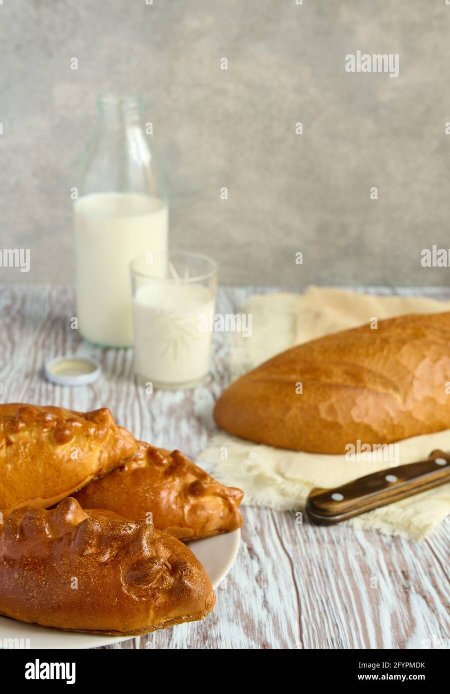 Pasteles rellenos, pan blanco y leche fresca en una botella de vidrio sobre una mesa de madera, profundidad de nitidez poco profunda Foto de stock