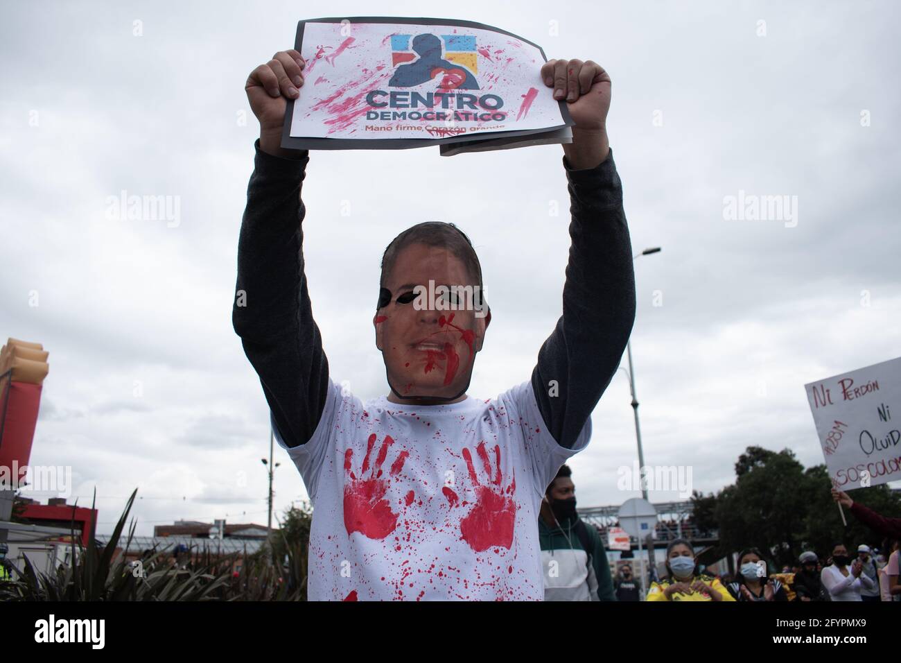 Un manifestante lleva una máscara de la cara del presidente Iván Duque, mientras sostiene una señal que dice: 'Centro demoníaco' en referencia al partido político colombiano Centro Democrático en un nuevo día de protestas en Bogotá en el contexto de la conmemoración de un mes de inicio de la huelga nacional en Colombia contra el Gobierno de Ivan Duque, el 28 de marzo de 2021. Foto de stock