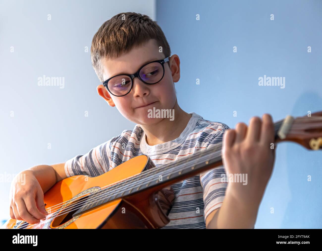 Lindo niño con gafas aprende a tocar la guitarra clásica en casa Fotografía  de stock - Alamy