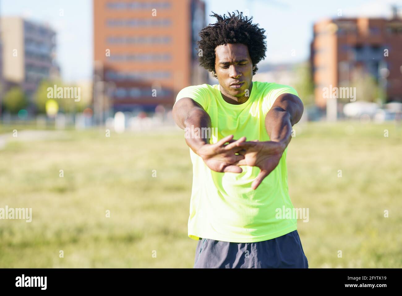 Hombre negro con pelo afro que se estira después de correr al aire libre. Foto de stock