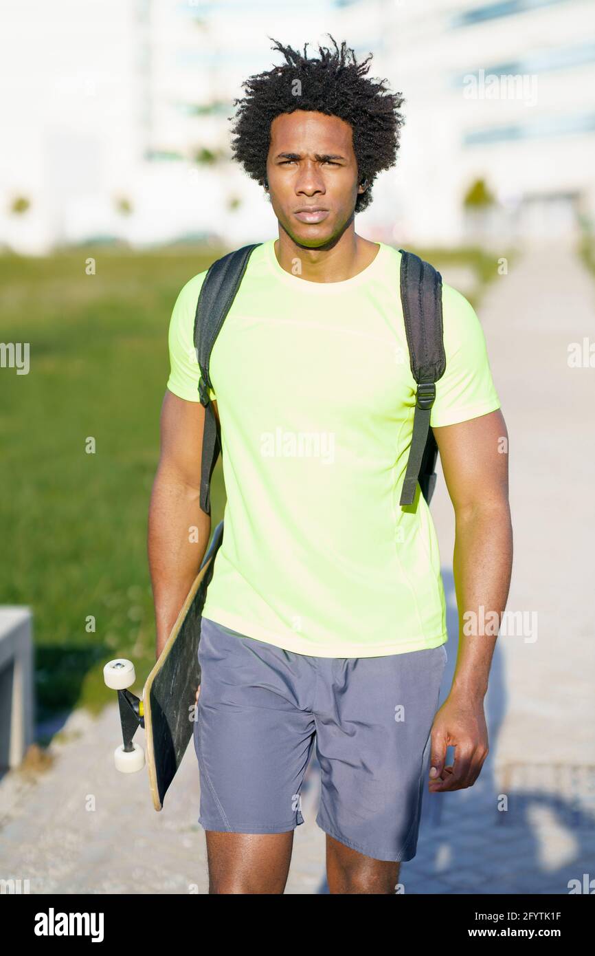 Hombre negro que va para un entrenamiento en ropa deportiva y un skateboard. Foto de stock