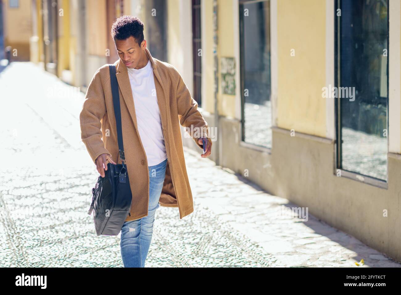 Joven negro caminando por la calle llevando un maletín y un smartphone. Foto de stock