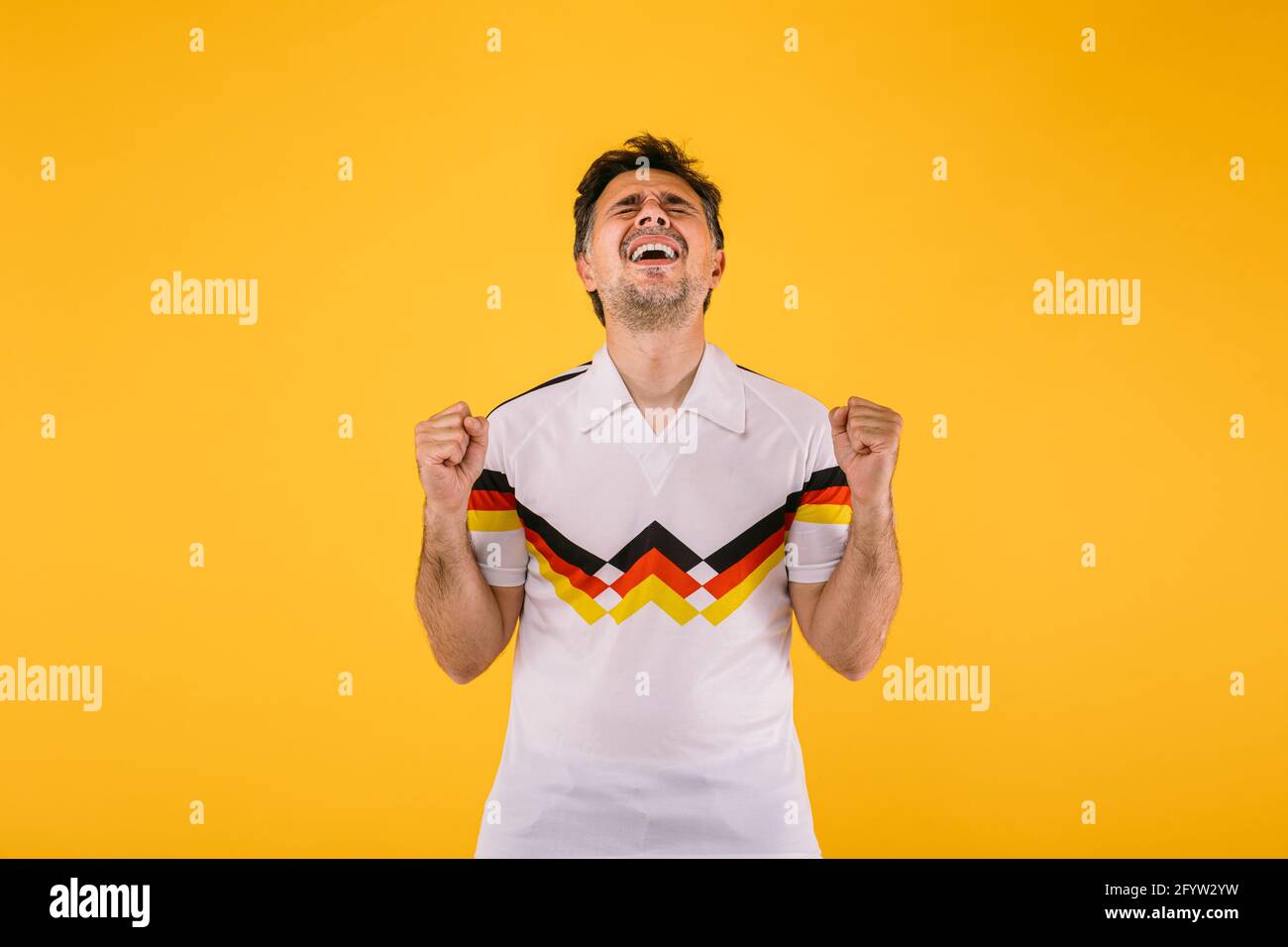 al fútbol que lleva una camiseta blanca con rayas negras, rojas amarillas, aplasta a sus puños y grita aclamando a equipo Fotografía de stock - Alamy