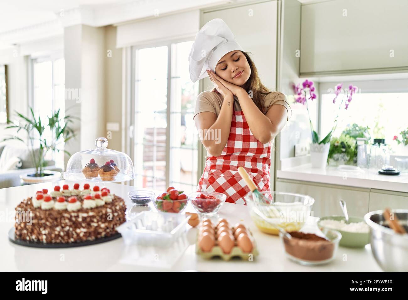 Hermosa joven mujer de pastelería de brunette chef cocina pasteles en el  cocina durmiendo cansado soñando y posando con las manos juntas mientras  sonriendo con c Fotografía de stock - Alamy