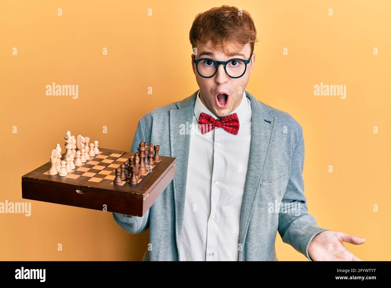 Joven caucásico con gafas sosteniendo un tablero de ajedrez asustado y  sorprendido con la boca abierta para sorpresa, cara incredulidad Fotografía  de stock - Alamy