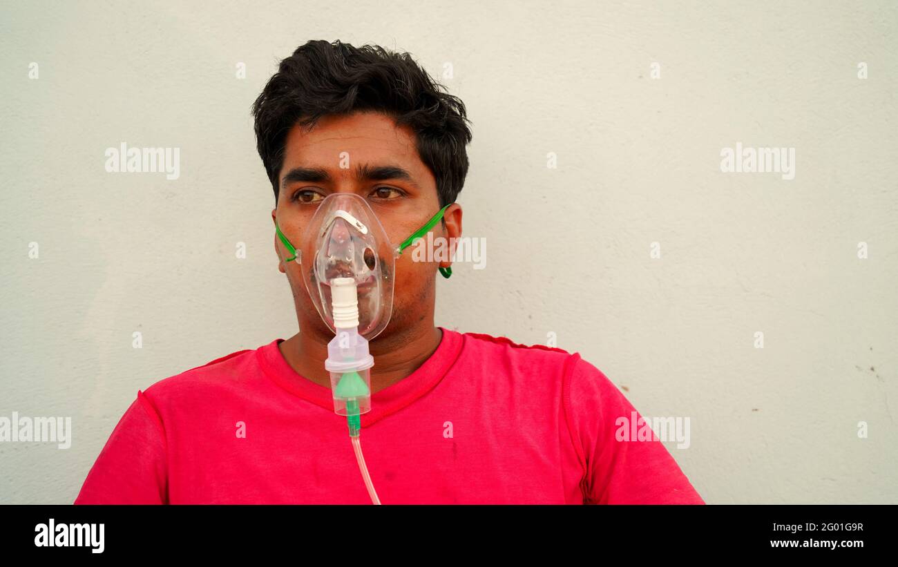 Un hombre indio con máscara de oxígeno en la cara en casa durante el encierro en Rajasthan, India. Persona joven sentada e inhalando oxígeno puro para el coronavirus A. Foto de stock