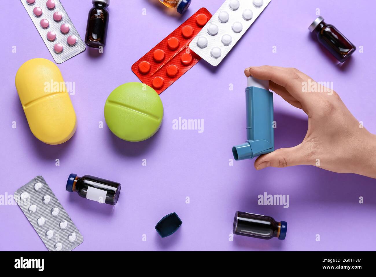 Mano femenina con inhalador y medicamentos sobre fondo de color Foto de stock