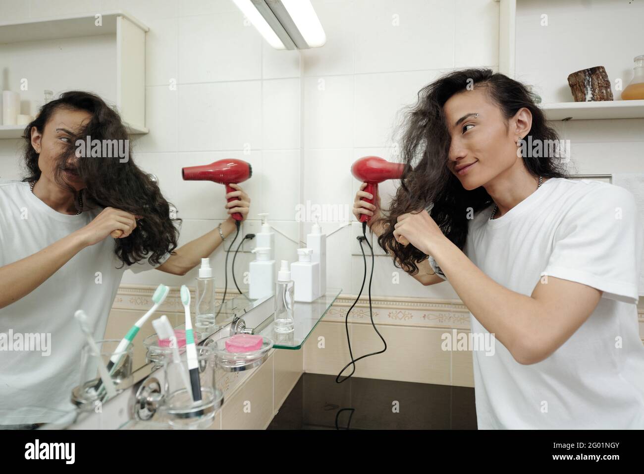 Hombre vietnamita joven sonriente con pelo largo en frente de espejo y  secador de pelo en el baño Fotografía de stock - Alamy