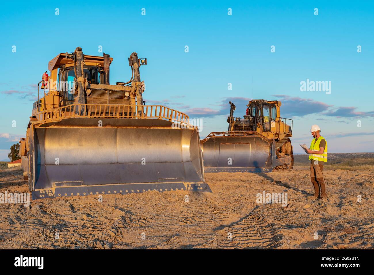 Inspector de construcción con casco de seguridad y chaleco reflectante tomando notas durante una inspección de maquinaria pesada en una construcción de carretera sitio Foto de stock