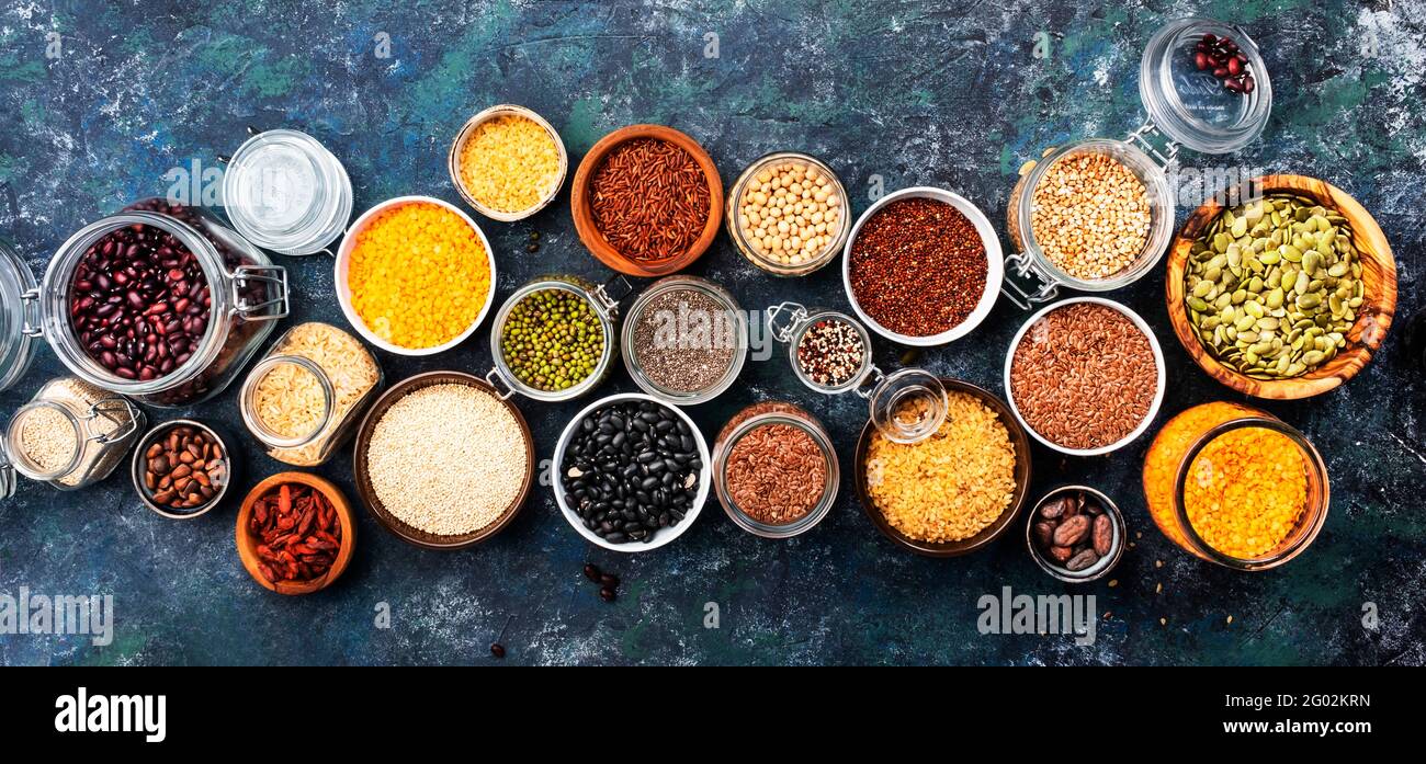 Diversos superalimentos orgánicos, frijoles, granos, cereales, legumbres, semillas en latas y tarros reutilizables. Vista superior del espacio de copia. Fondo azul Foto de stock