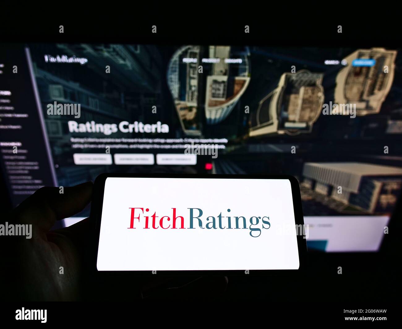 Persona que sostiene el smartphone con el logotipo de la agencia de calificación crediticia estadounidense Fitch Ratings Inc. En la pantalla frente al sitio web de la empresa. Enfoque en la pantalla del teléfono. Foto de stock