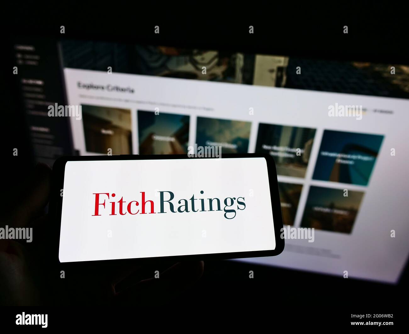 Persona que sostiene el teléfono móvil con el logotipo de la agencia estadounidense de calificación de crédito Fitch Ratings Inc. En la pantalla frente a la página web. Enfoque en la pantalla del teléfono. Foto de stock