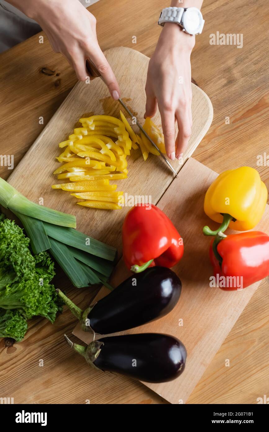 vista superior de las manos femeninas picado de pimienta amarilla en la tabla de cortar en la mesa de la cocina Foto de stock