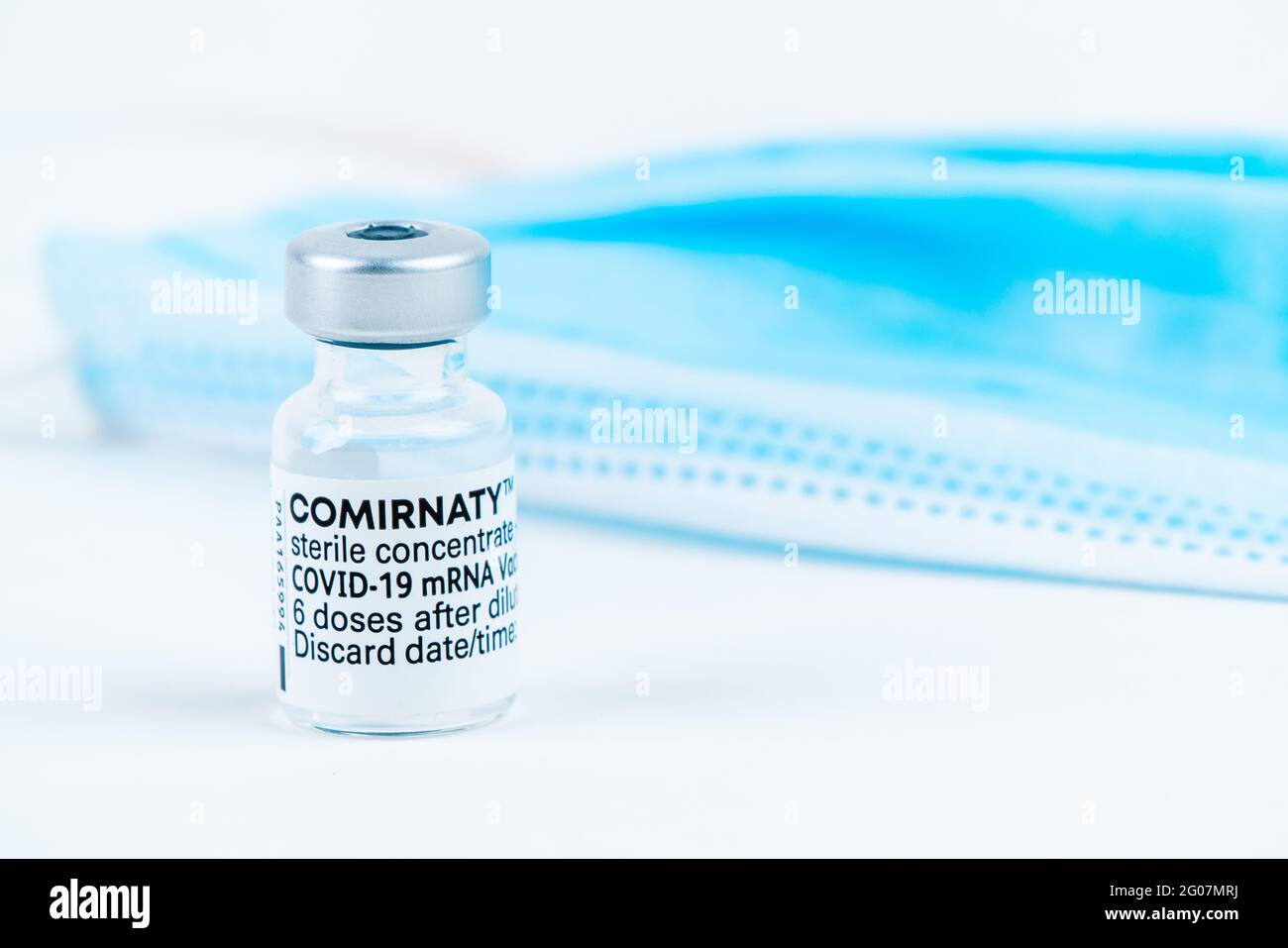 Celadna, República Checa - 05.30.2021: Ampolla de la vacuna Comirnaty de Pfizer sobre fondo blanco, con máscara azul al lado Foto de stock