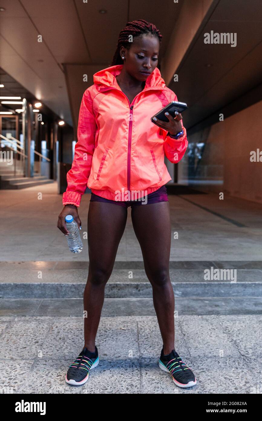 Deportista afroamericana deportiva con chaqueta roja en la calle y  smartphone Fotografía de stock - Alamy
