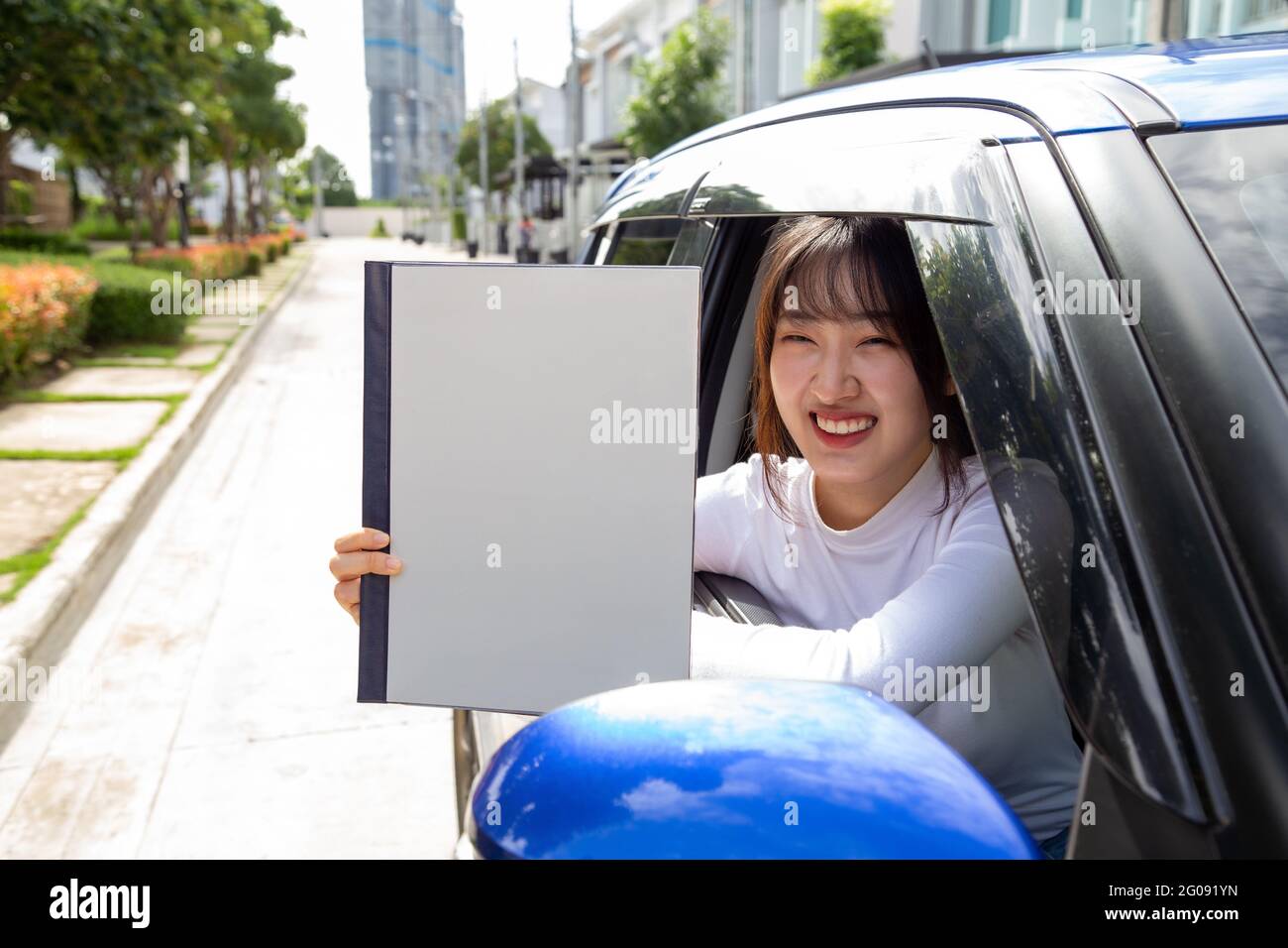 Mujer asiática joven que sostiene el libro de la póliza del coche y que se sienta en coche, concepto del seguro personal del accidente Foto de stock