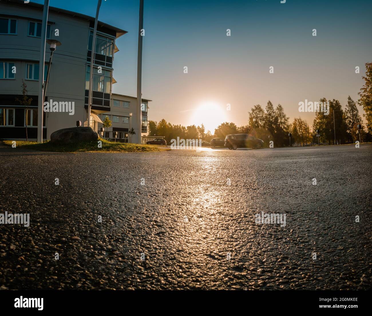 Vista panorámica de bajo nivel sobre el sol en aumento sobre el aparcamiento vacío cerca del típico edificio de oficinas, temprano por la mañana, cielo despejado con el amanecer detrás del color de otoño Foto de stock