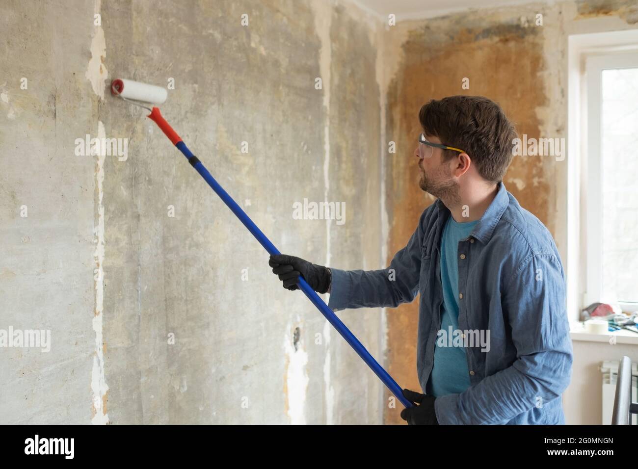 Hombre caucásico pintando paredes de cemento con cepillo de rodillo y  imprimador haciendo una renovación Fotografía de stock - Alamy