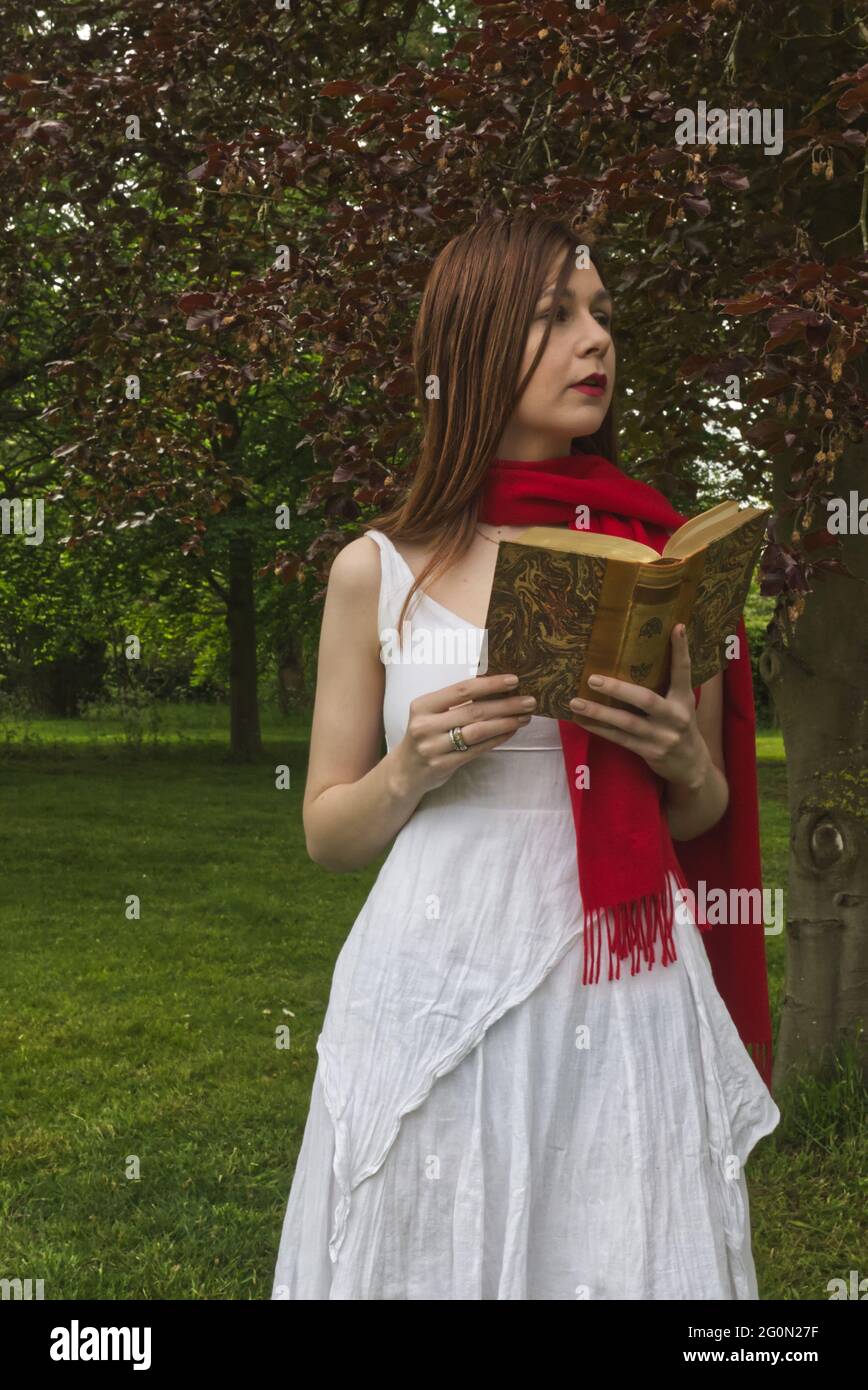 Mujer de vestido blanco y rojo escarfe leyendo un libro en el jardín  mientras está de pie Fotografía de stock - Alamy