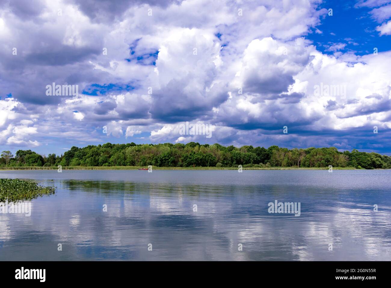 Con vistas a un lago rural de Wisconsin, el lago Asippun, en el condado de Waukesha. Las nubes cumulus se reflejan en las aguas tranquilas. La costa está cubierta por Foto de stock