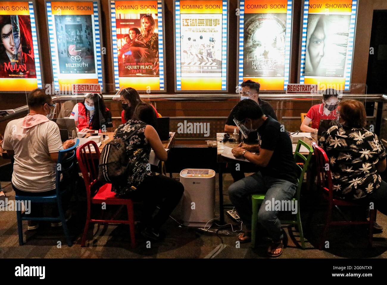 Las personas que usan máscaras protectoras y protectores faciales se registran antes de recibir su dosis de la vacuna Sinovac COVID-19 dentro de un cine convertido en un sitio de vacunación en la ciudad de San Juan, Metro Manila, Filipinas. Foto de stock