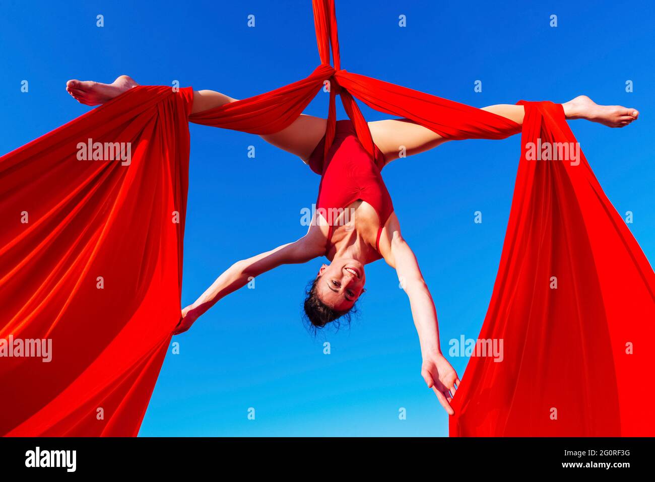 acróbata deportiva, elegante gimnasta realizando ejercicio aéreo con telas  rojas al aire libre sobre fondo del cielo. mujer flexible en traje rojo  interpreta circo Fotografía de stock - Alamy