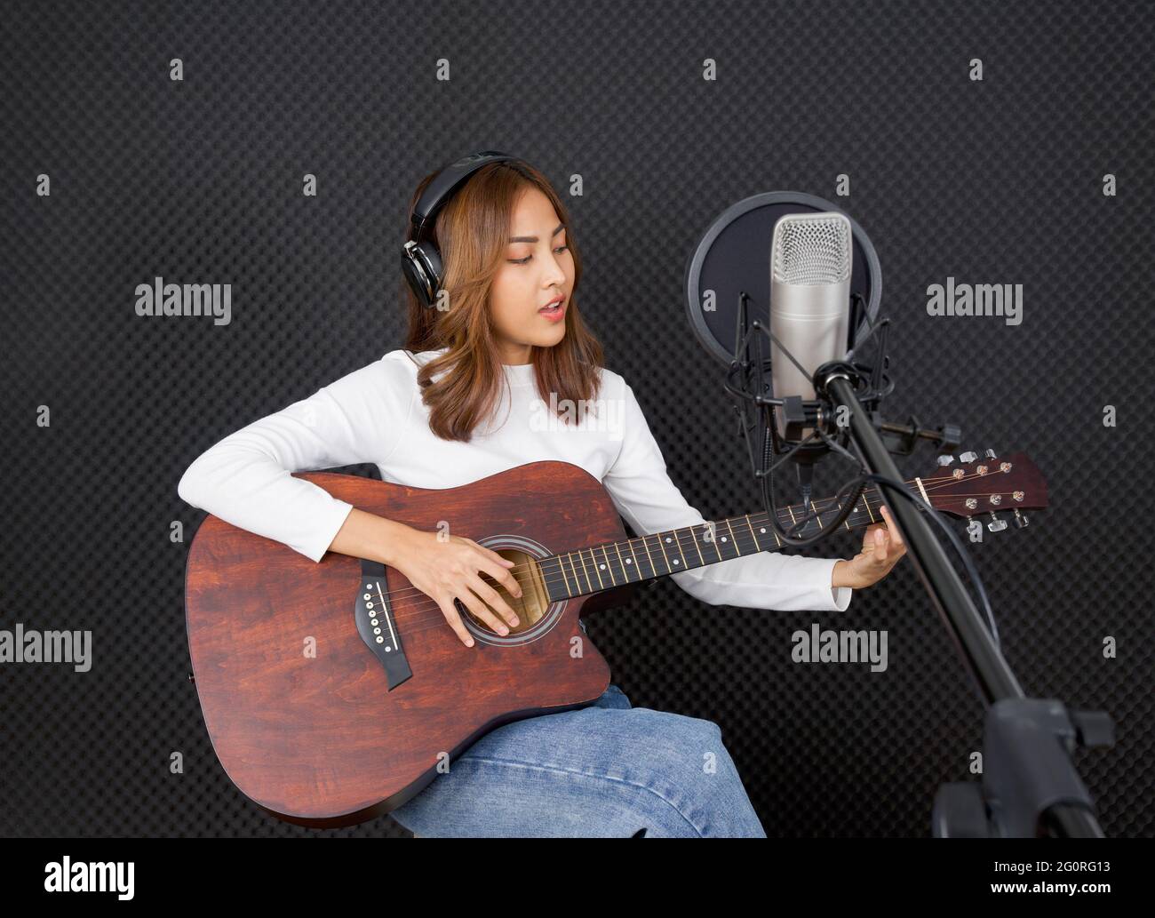 Una joven asiática con auriculares canta mientras toca una guitarra acústica  frente a la pared de insonorización negra. Músico que produce música en  profesional Fotografía de stock - Alamy