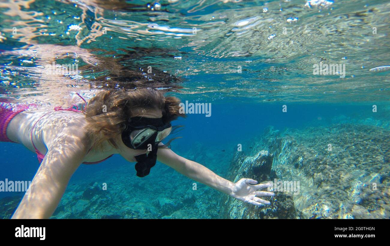 Una niña buceando y explorando el entorno rocoso bajo el agua y los corales. Foto de stock