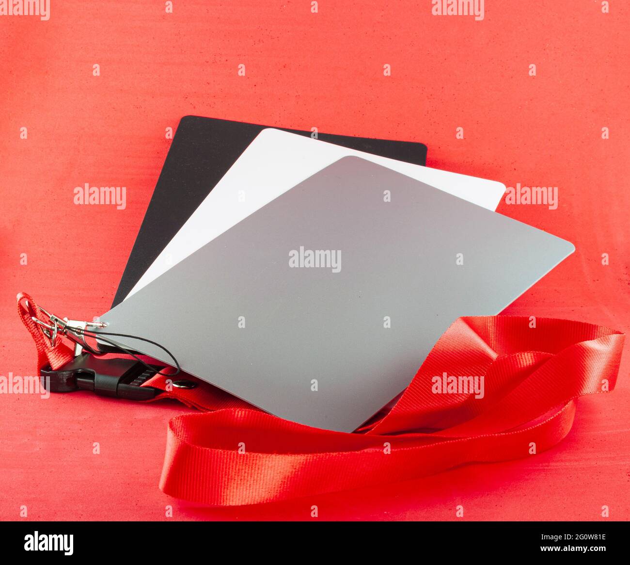 Tarjetas grises para fotógrafos colocados sobre un fondo rojo. Hay tres cartas, una gris, una blanca y una negra. Están unidos con un gancho y un Foto de stock