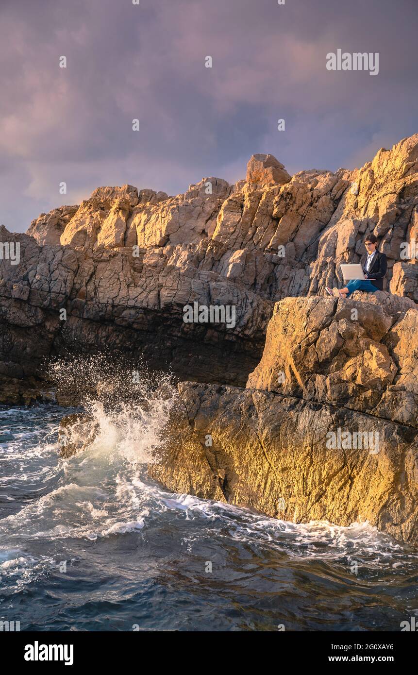 Mujer sentada en la roca sobre el mar y trabajando en la computadora. Mujer de negocios trabajando desde la playa. Concepto de trabajo a distancia. Tra. Independiente Foto de stock