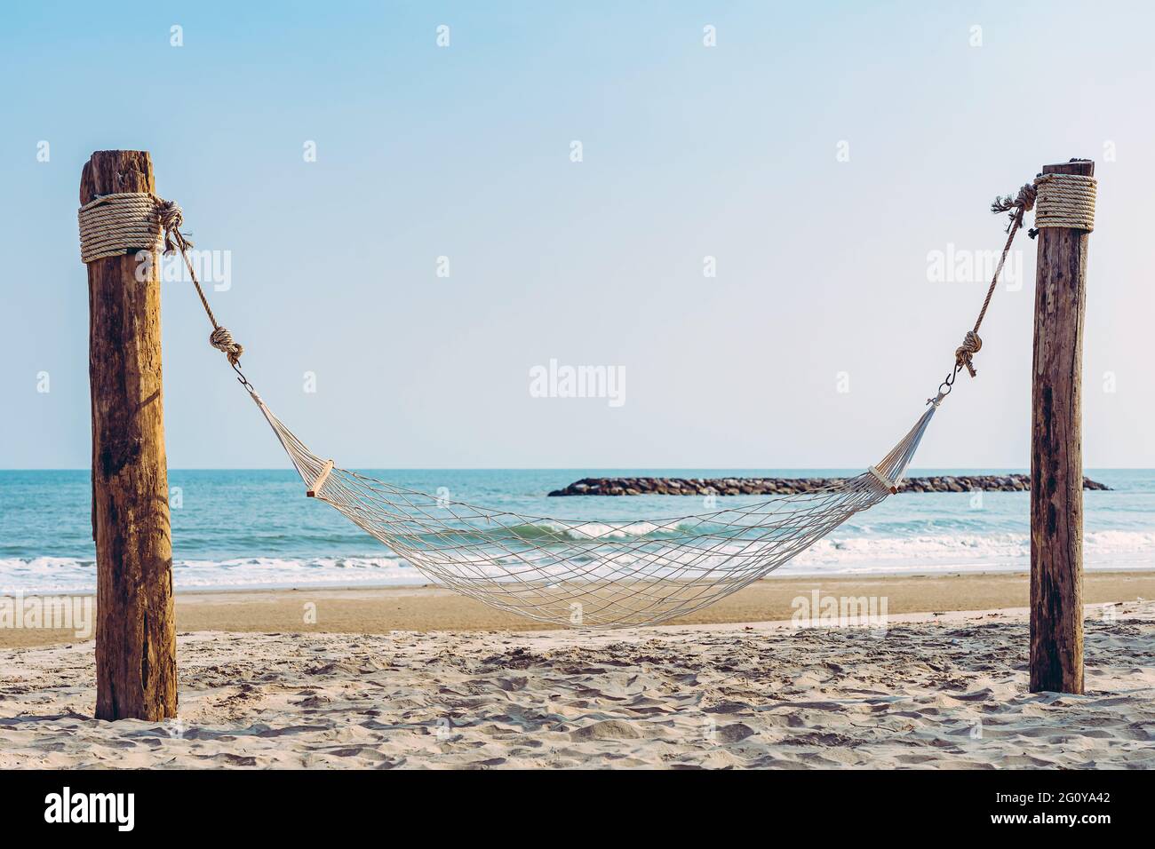 Hamaca acogedora vacía hecha de malla colgada en postes de madera en la  playa blanca tropical para los turistas. Playa de arena de verano con hamaca  en el mar borroso y el