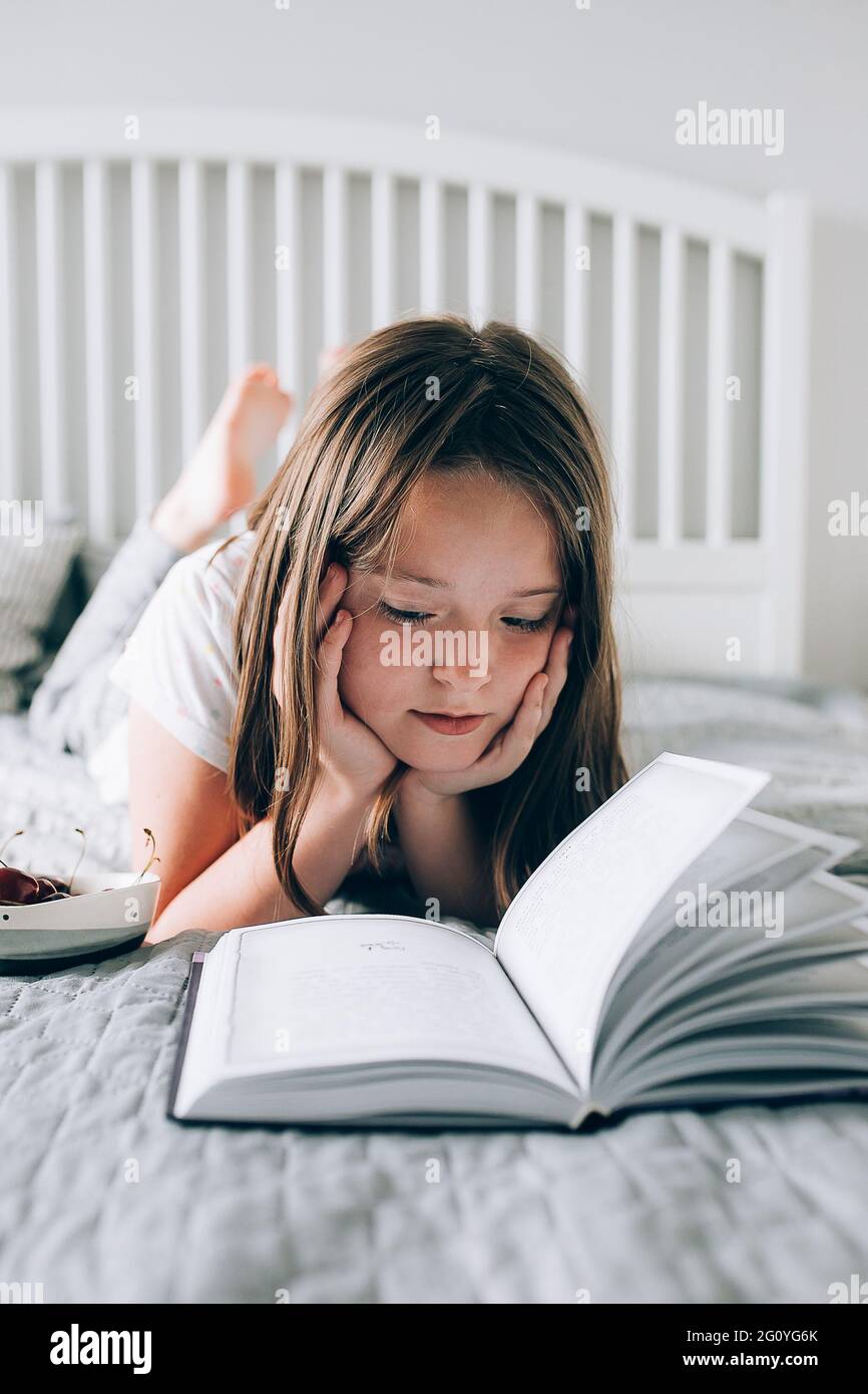 Bonita niña de 8-9 años se encuentra en la cama, leyendo el libro
