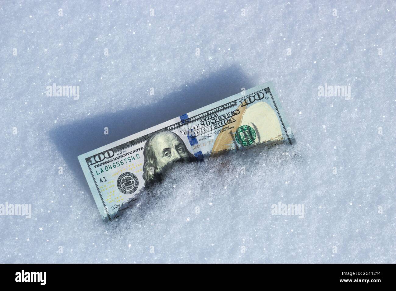 La moneda estadounidense está en la nieve. Cien dólares en la nieve. Foto de stock