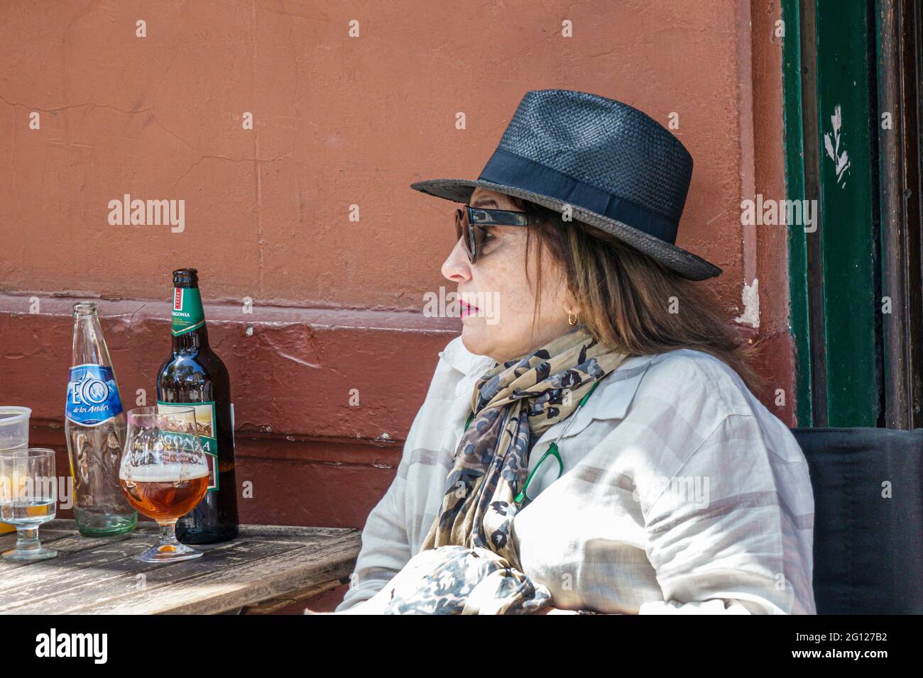 Argentina Buenos Aires San Telmo Plaza Dorrego mesa de café al aire libre mujer hispana con sombrero fedora gafas de sol beber cerveza botella de vidrio Foto de stock