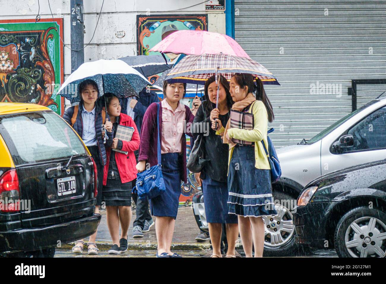 Argentina Buenos Aires San Telmo centro histórico grupo de mujeres asiáticas turistas sosteniendo paraguas cruzando la calle lluvia lloviendo día lluvioso Foto de stock