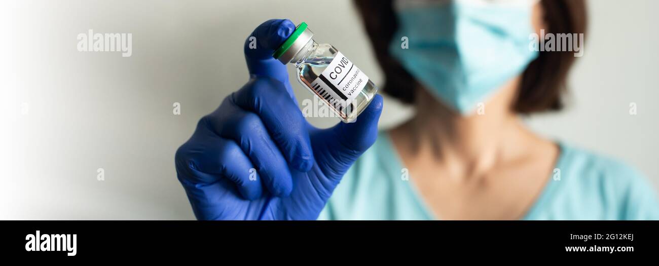 Enfermera de mediana edad en máscara de seguridad y guantes sostiene el frasco con la vacuna líquida COVID para inyecciones. Foto de stock