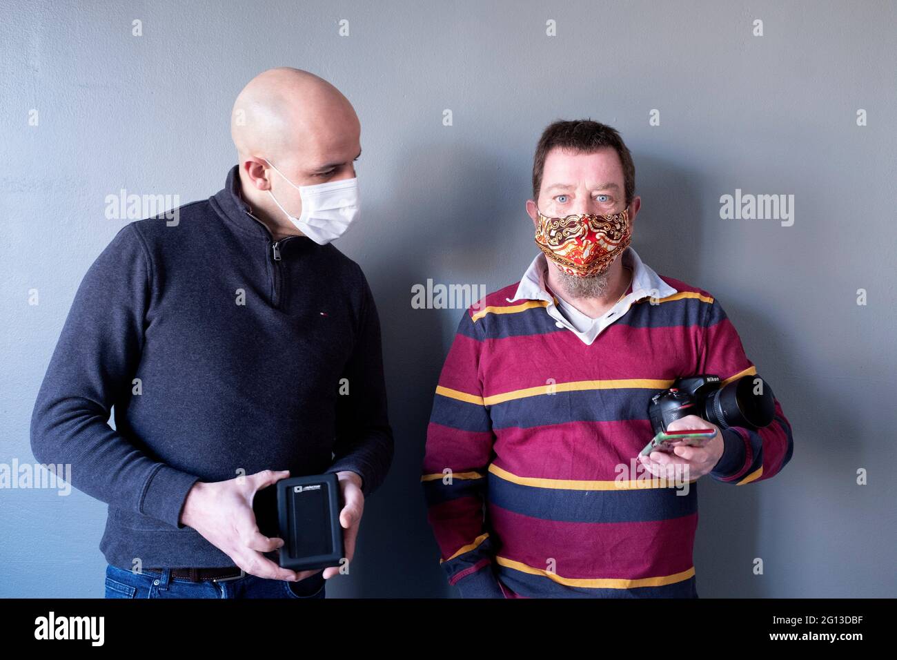 Tilburg, Países Bajos. Doble retrato de dos profesionales, machos caucásicos, uno sosteniendo una cámara y iPhone 11 Remote, el otro sosteniendo su almacenamiento Foto de stock