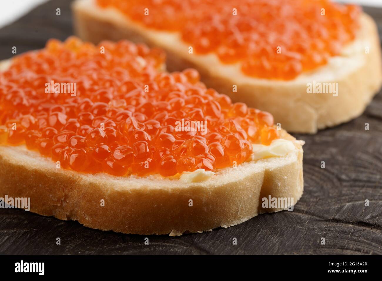 Dos panes con huevas de salmón rojo sobre plato de madera Foto de stock