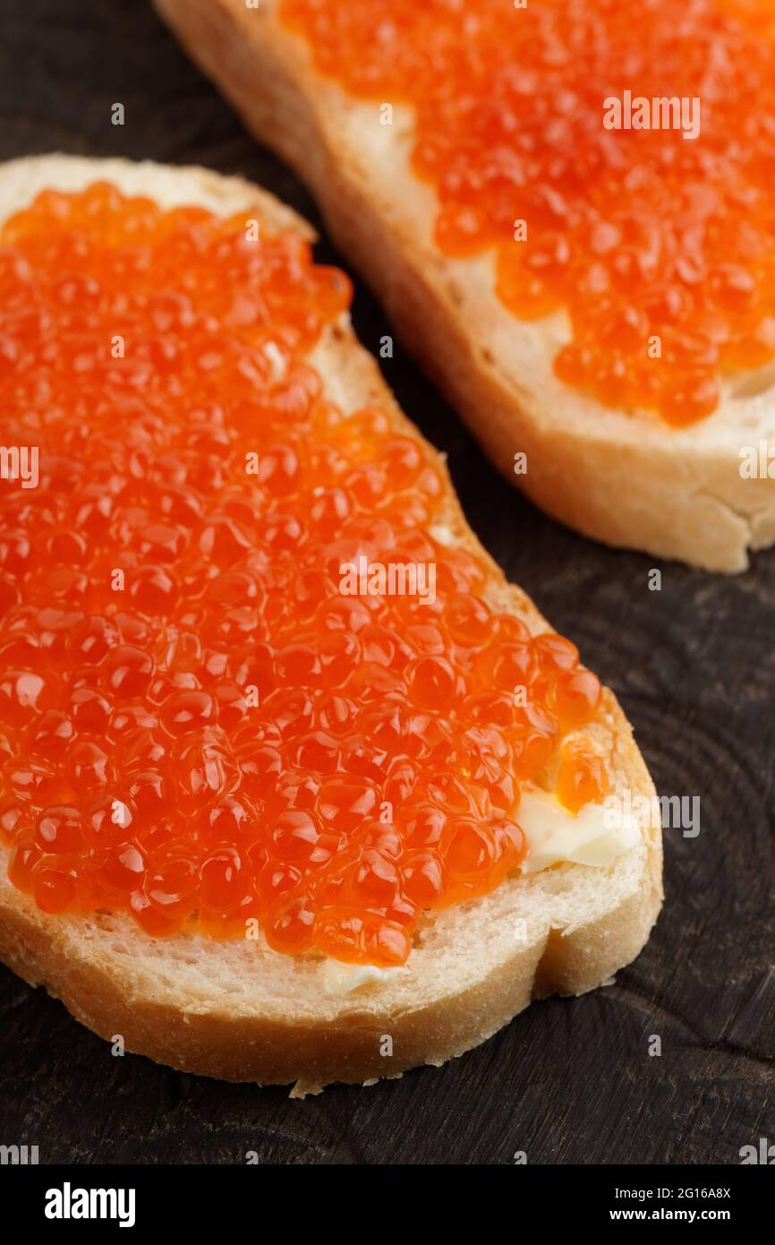 Dos panes con huevas de salmón rojo sobre plato de madera Foto de stock