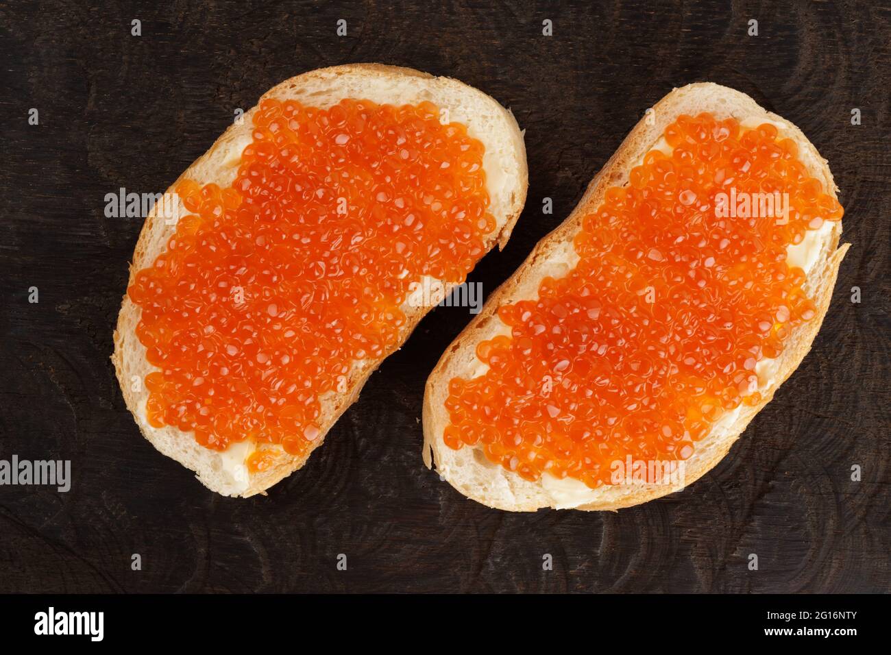 Dos panes con huevas de salmón sobre tabla de madera rodada desde arriba Foto de stock