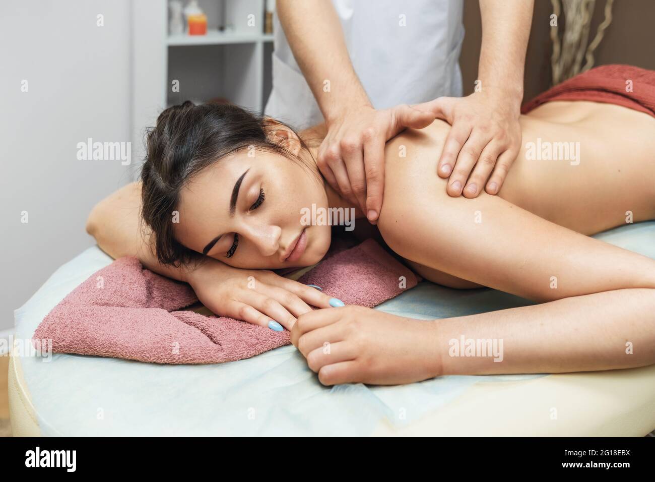 Joven hermosa mujer morena en un salón de spa está descansando durante una sesión de masaje en los músculos del trapecio y la región cervical. Foto de stock